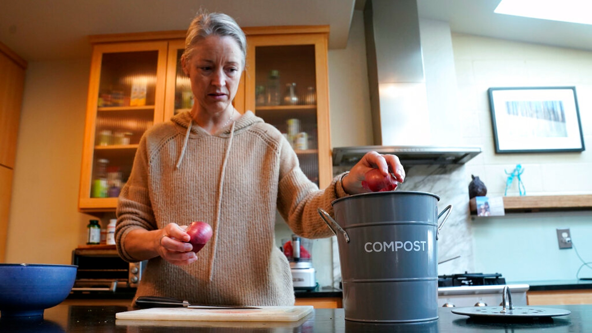 Joy Klineberg tosses an onion peel into container to be used for composting while preparing a family meal at her home in Davis, Calif., Tuesday, Nov. 30, 2021. (AP Photo/Rich Pedroncelli)