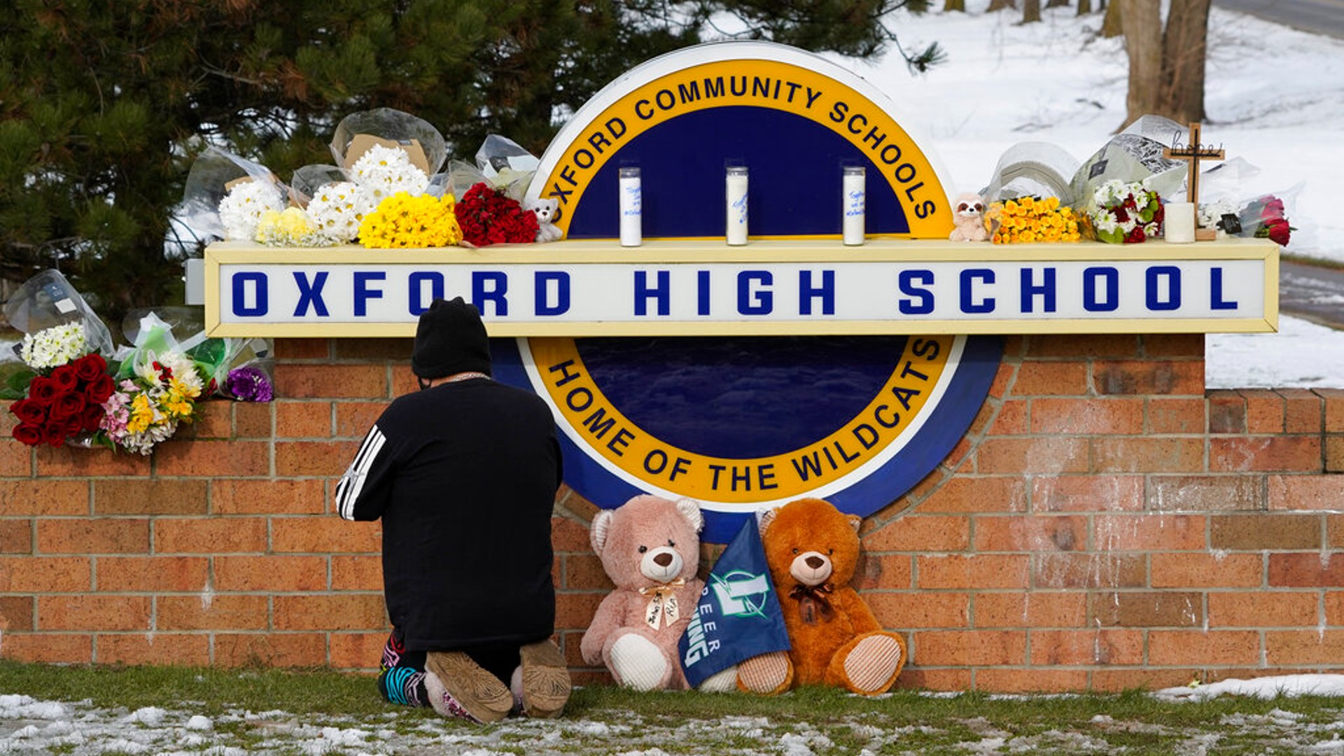 A well wisher kneels to pray at a memorial on the sign of Oxford High School in Oxford, Mich., Wednesday, Dec. 1, 2021. (AP Photo/Paul Sancya)