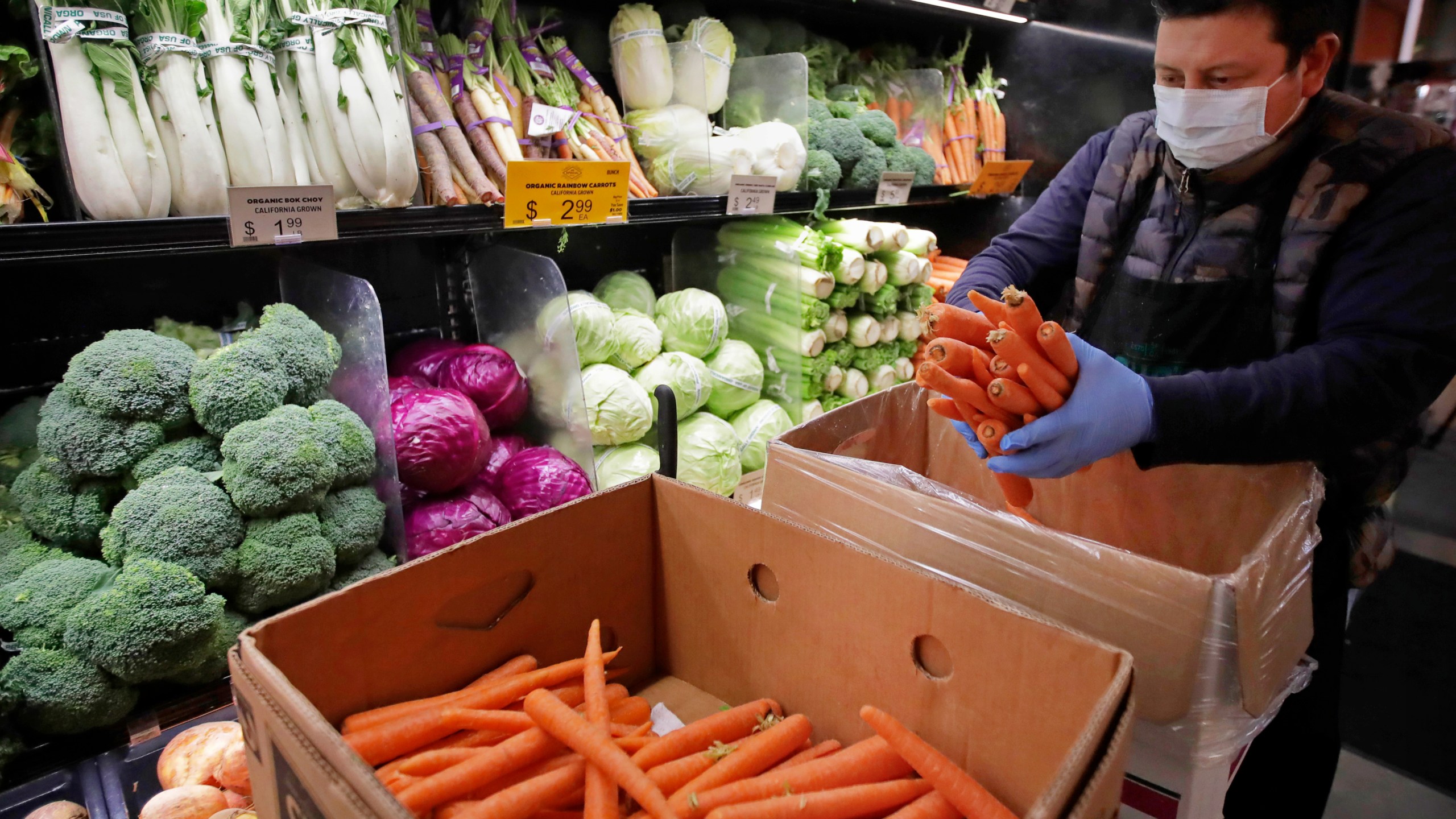 In this March 27, 2020, file photo, a worker, wearing a protective mask against the coronavirus, stocks produce before the opening of Gus's Community Market in San Francisco. (AP Photo/Ben Margot, File)