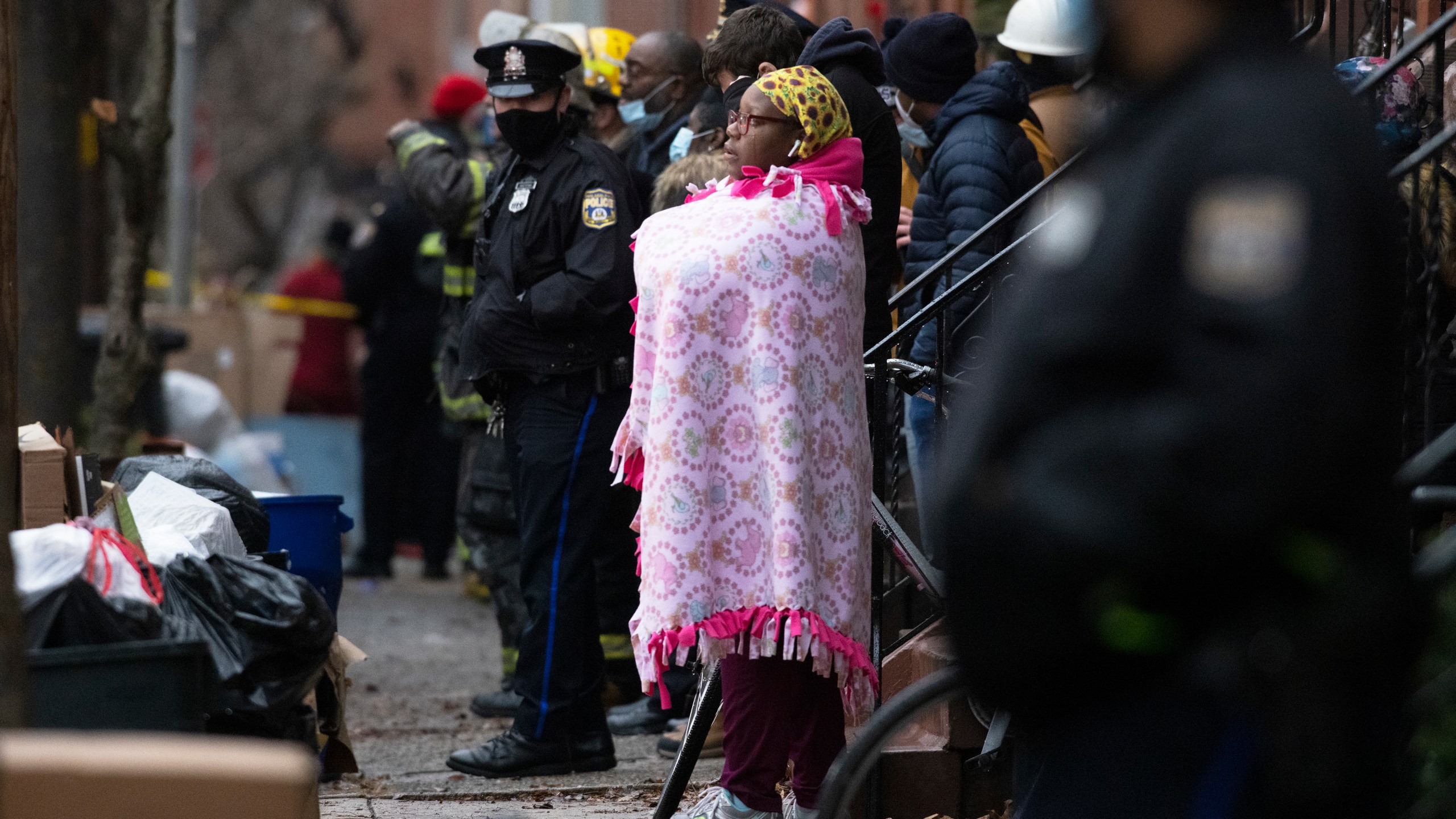 Bystanders watch as the Philadelphia fire department works at the scene of a deadly row house fire in Philadelphia on Wednesday, Jan. 5, 2022. Firefighters and police responded to the fatal fire at a three-story rowhouse in the city's Fairmount neighborhood around 6:40 a.m. and found flames coming from the second-floor windows, fire officials said. (Alejandro A. Alvarez/The Philadelphia Inquirer via AP)