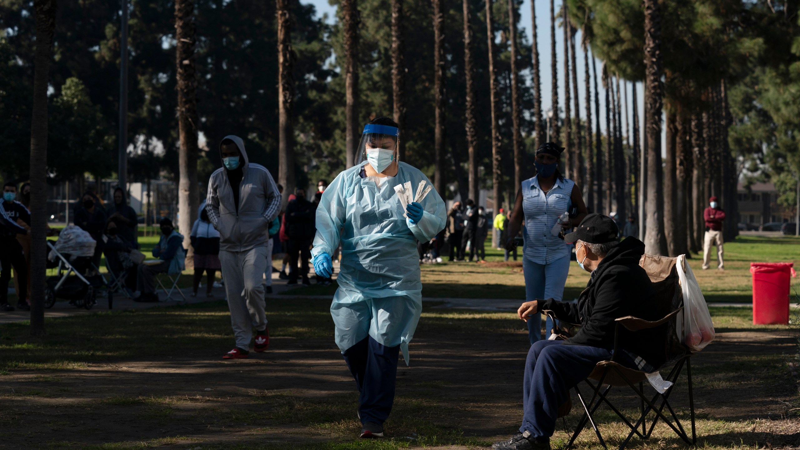 Medical assistant Leslie Powers, center, carries swab samples collected from people to process them on-site as people wait in line for a test at a COVID-19 testing site in Long Beach, Calif., Thursday, Jan. 6, 2022. (AP Photo/Jae C. Hong)