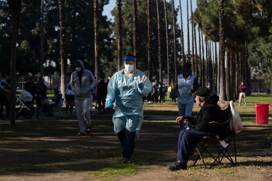 Medical assistant Leslie Powers, center, carries swab samples collected from people to process them on-site as people wait in line for a test at a COVID-19 testing site in Long Beach, Calif., Thursday, Jan. 6, 2022. (AP Photo/Jae C. Hong)