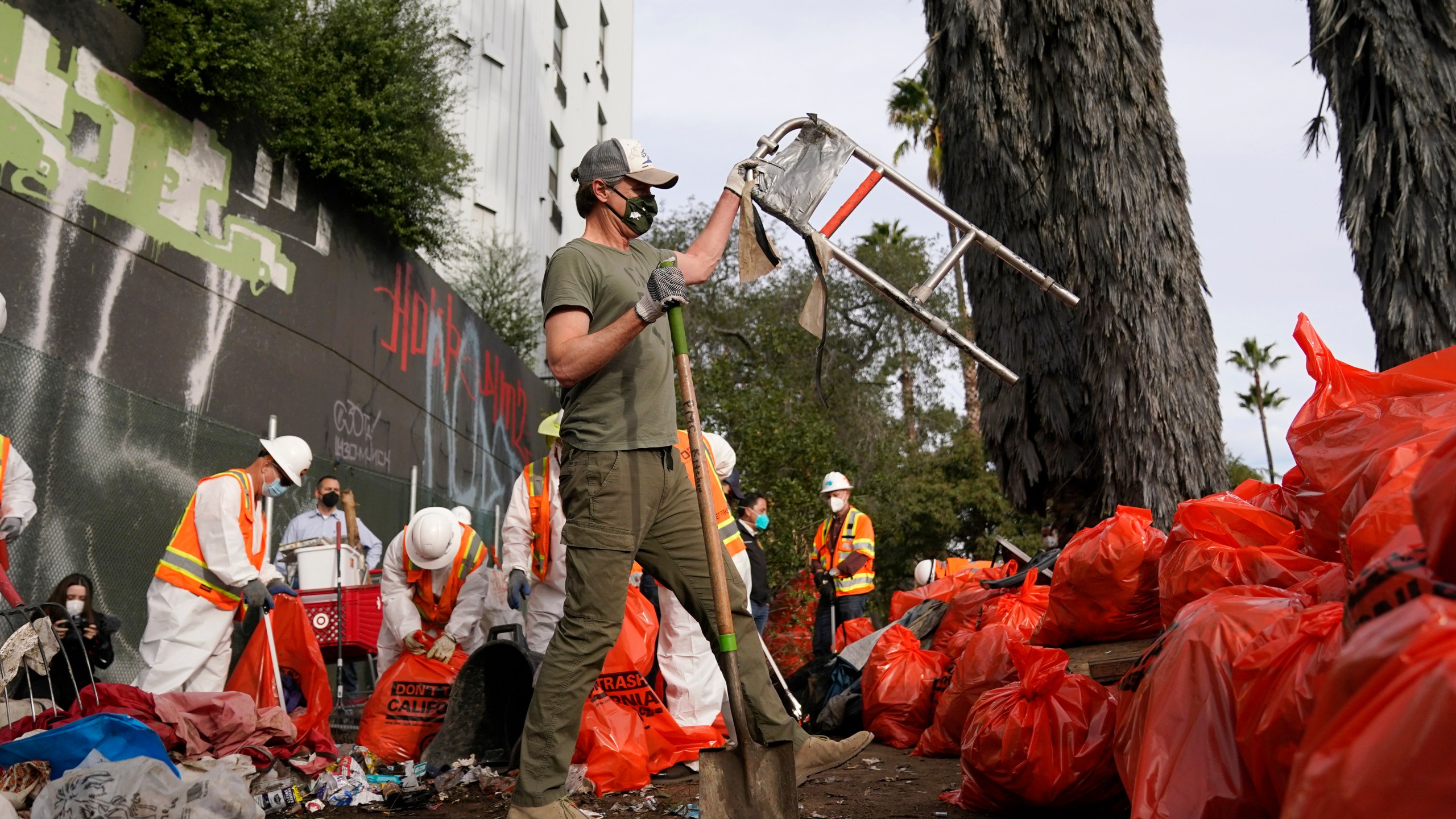 California Gov. Gavin Newsom, center, helps clean a homeless encampment alongside a freeway on Jan. 12, 2022, in San Diego. (AP Photo/Gregory Bull)