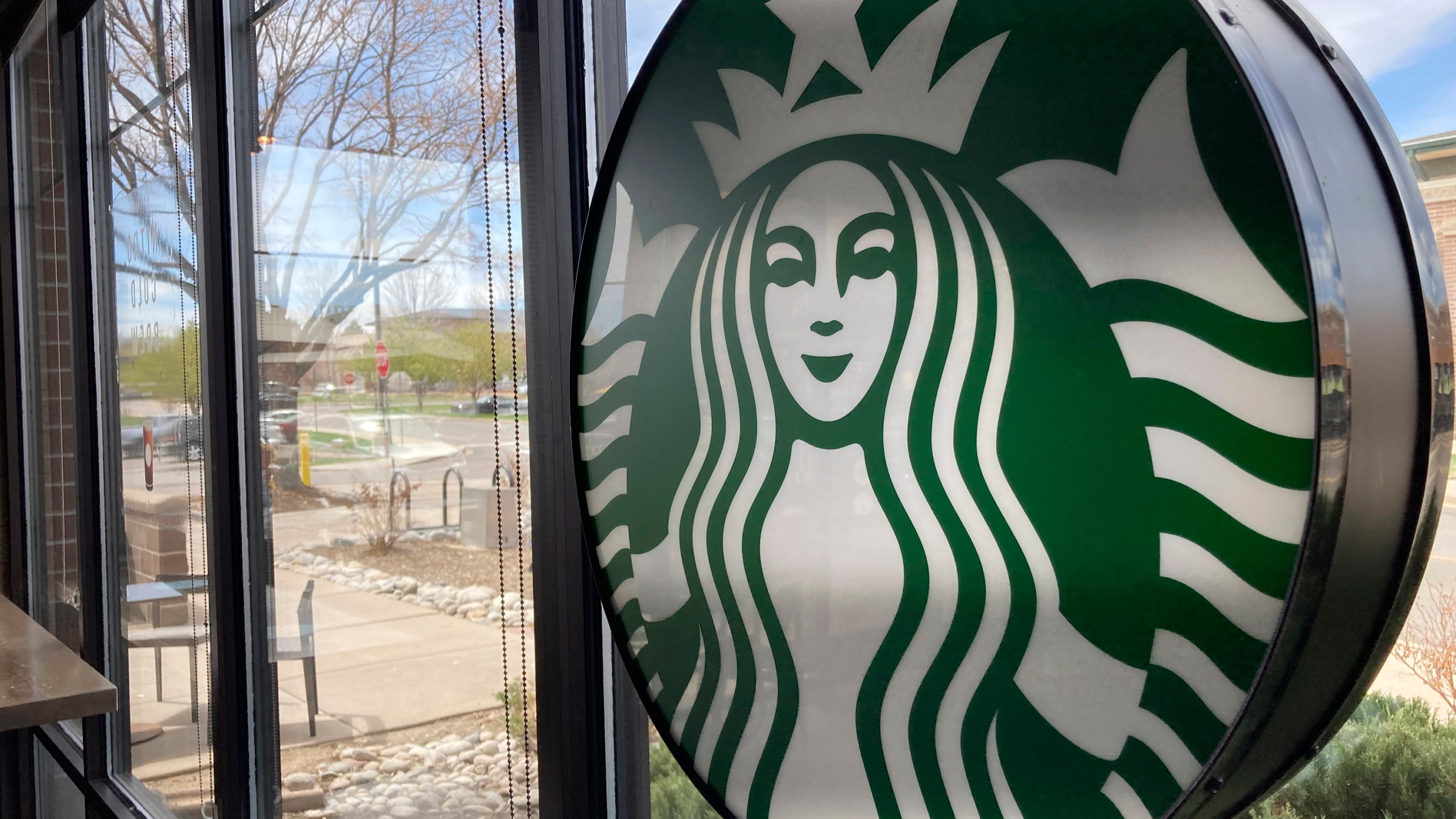 A sign bearing the corporate logo hangs in the window of a Starbucks open only to take-away customers in this photograph taken Monday, April 26, 2021, in southeast Denver. Starbucks is no longer requiring its U.S. workers to be vaccinated against COVID-19, reversing a policy it announced earlier this month. The Seattle coffee giant says, Wednesday, Jan. 19, 2022, it's responding to last week’s ruling by the U.S. Supreme Court. (AP Photo/David Zalubowski)