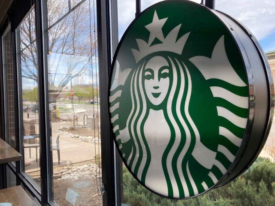 A sign bearing the corporate logo hangs in the window of a Starbucks open only to take-away customers in this photograph taken Monday, April 26, 2021, in southeast Denver. Starbucks is no longer requiring its U.S. workers to be vaccinated against COVID-19, reversing a policy it announced earlier this month. The Seattle coffee giant says, Wednesday, Jan. 19, 2022, it's responding to last week’s ruling by the U.S. Supreme Court. (AP Photo/David Zalubowski)