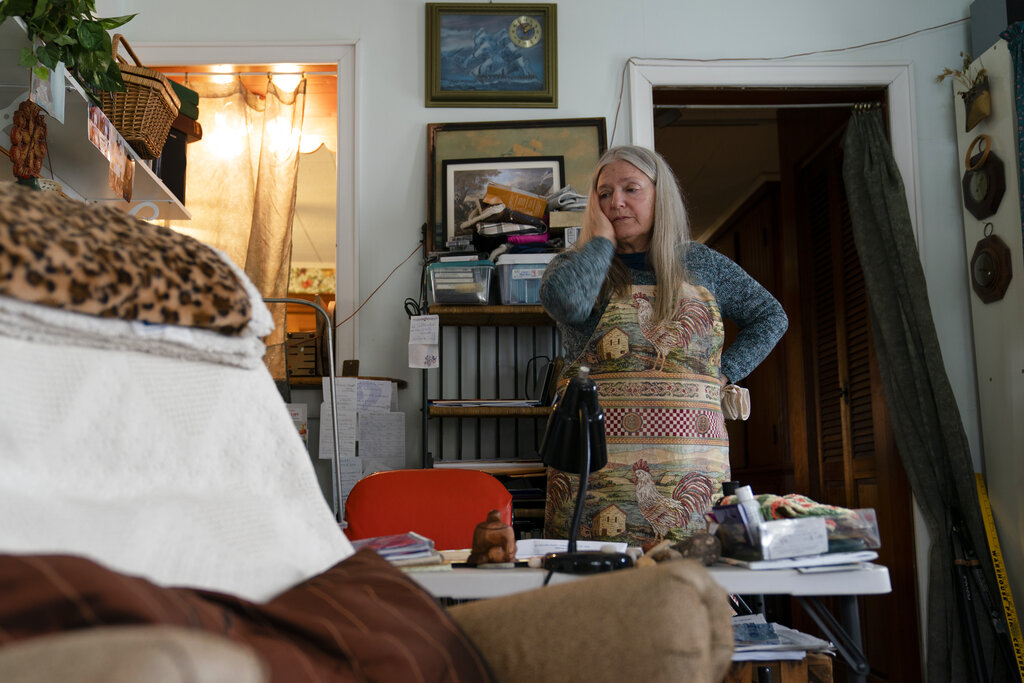 Nancy Rose, who contracted COVID-19 in 2021 and continues to exhibit long-haul symptoms including brain fog and memory difficulties, pauses while organizing her desk space, Tuesday, Jan. 25, 2022, in Port Jefferson, N.Y. (AP Photo/John Minchillo)