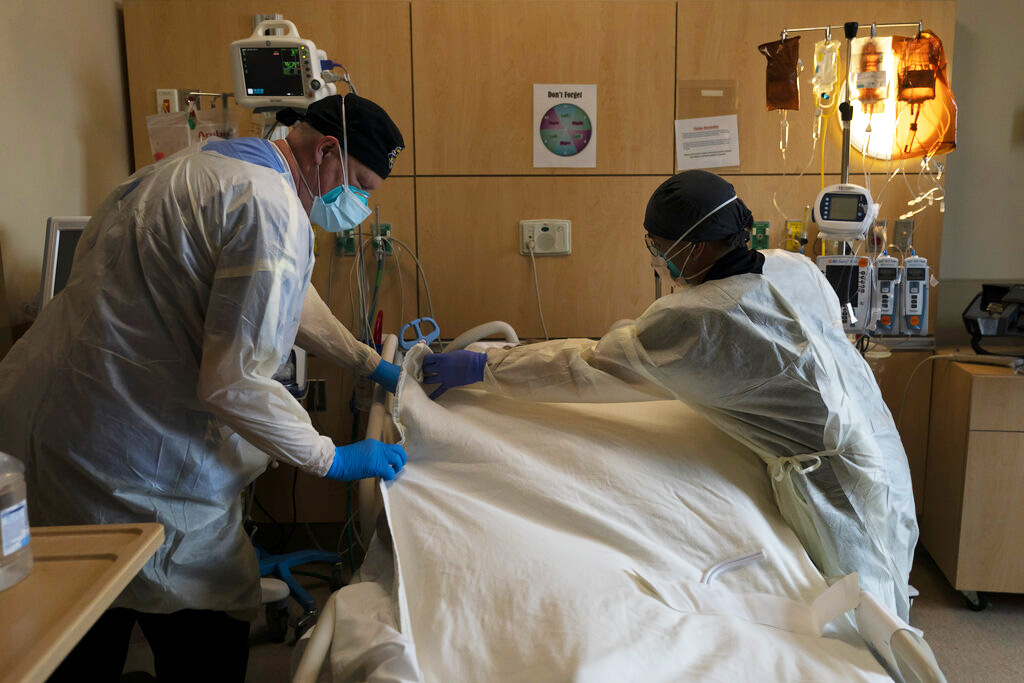 Respiratory therapist Frans Oudenaar, left, and registered nurse Bryan Hofilena cover a body of a COVID-19 patient with a sheet at Providence Holy Cross Medical Center in Los Angeles, Dec. 14, 2021. (AP Photo/Jae C. Hong, File)