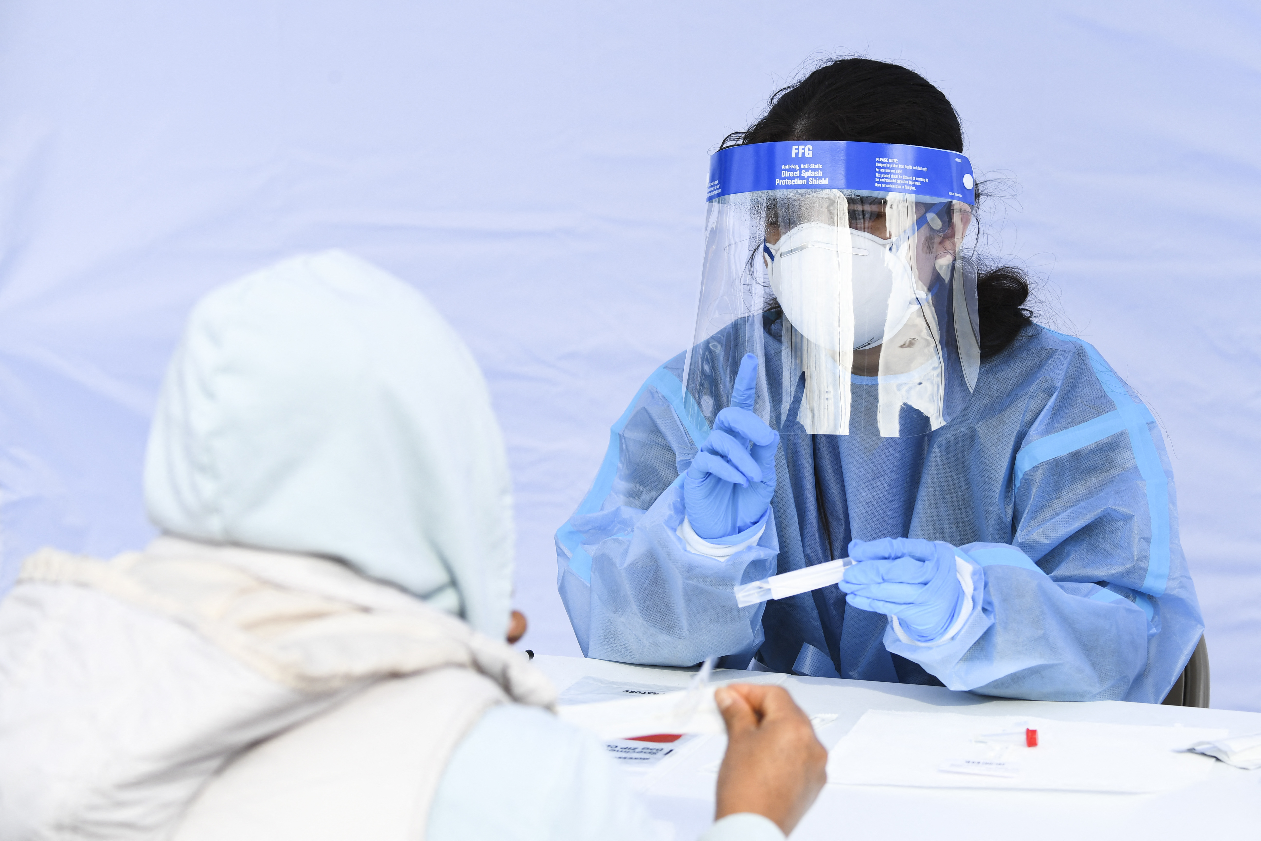 A healthcare worker gives instructions to a person on how to swab their nose as they receive testing for both rapid antigen and PCR COVID-19 tests at a Reliant Health Services testing site in Hawthorne on Jan. 18, 2022. (Patrick T. FALLON / AFP via Getty Images)