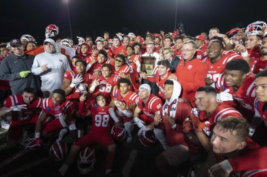 Father Walter E. Jenkins, wearing a red jacket, poses with the Mater Dei High varsity football team after a victory on Nov. 26. (Kyusung Gong)