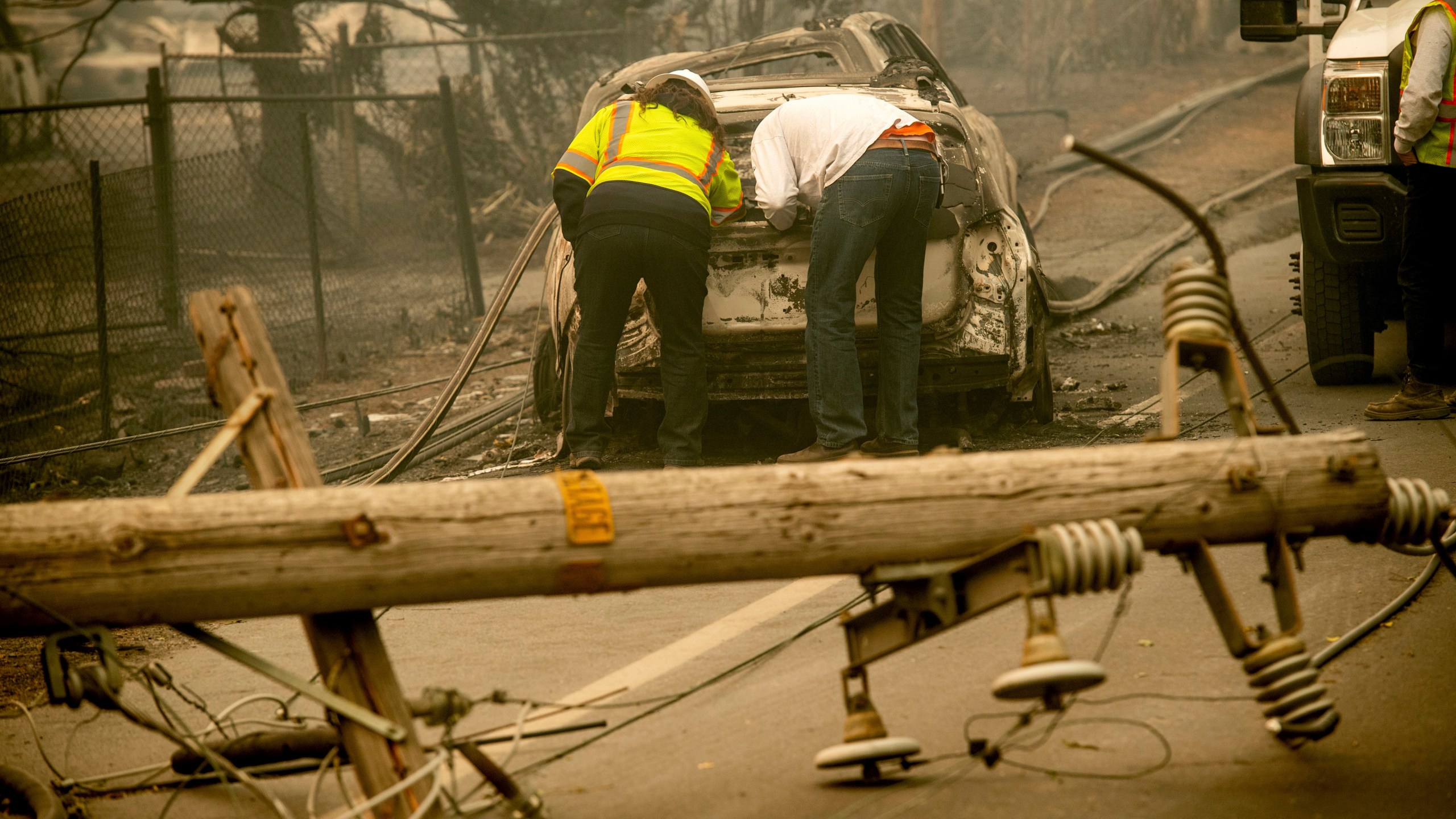 In this Nov. 10, 2018 file photo, with a downed power utility pole in the foreground, Eric England, right, searches through a friend's vehicle after the wildfire burned through Paradise, Calif. The nation's largest utility, Pacific Gas & Electric is poised to emerge from five years of criminal probation amid worries that it remains too dangerous to be trusted. Over the five years, the utility became an even more destructive force. More than 100 people have died and thousands of homes and businesses have been incinerated in wildfires sparked by its equipment in that time. (AP Photo/Noah Berger, File)