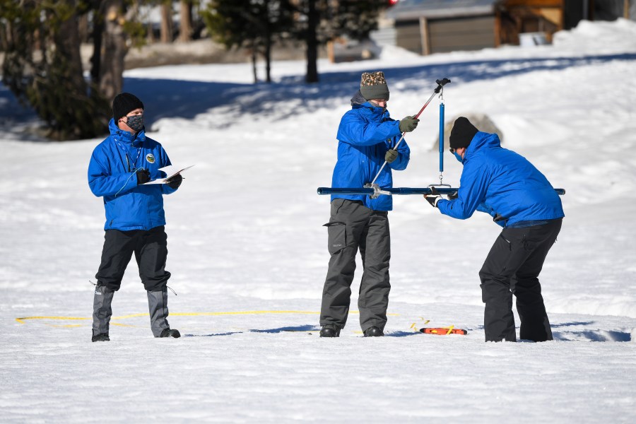 Sean de Guzman, chief of snow surveys for the California Department of Water Resources, right, places the snowpack measuring tube of a scale held by DWR's Anthony Burdock, center, as DWR's Andy Reising, left, looks on during the second snow survey of the season held at Phillips Station near Echo Summit, Calif., Tuesday, Feb. 1, 2022. The survey found the snowpack at 48.5 inches with 19 inches of snow water content. That's 109% of the historical average at this time of the year. But statewide, the water in the snowpack is 92%. (Kenneth James / California Department of Water Resources via AP)