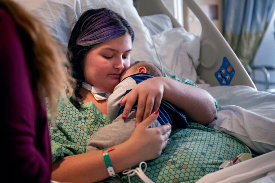 In this image provided by Kata Sasvari, Macenzee Keller, 20, of Manchester, N.H., clutches her two-month-old son Zachery for the first time since she giving birth, at the Dartmouth-Hitchcock Medical Center in Lebanon, N.H., Feb. 3, 2022. Keller delivered Zachery on Nov. 28, 2021, while on a ventilator at Catholic Medical Center in Manchester. N.H., after being stricken with COVID-19. (Kata Sasvari photograph via AP)