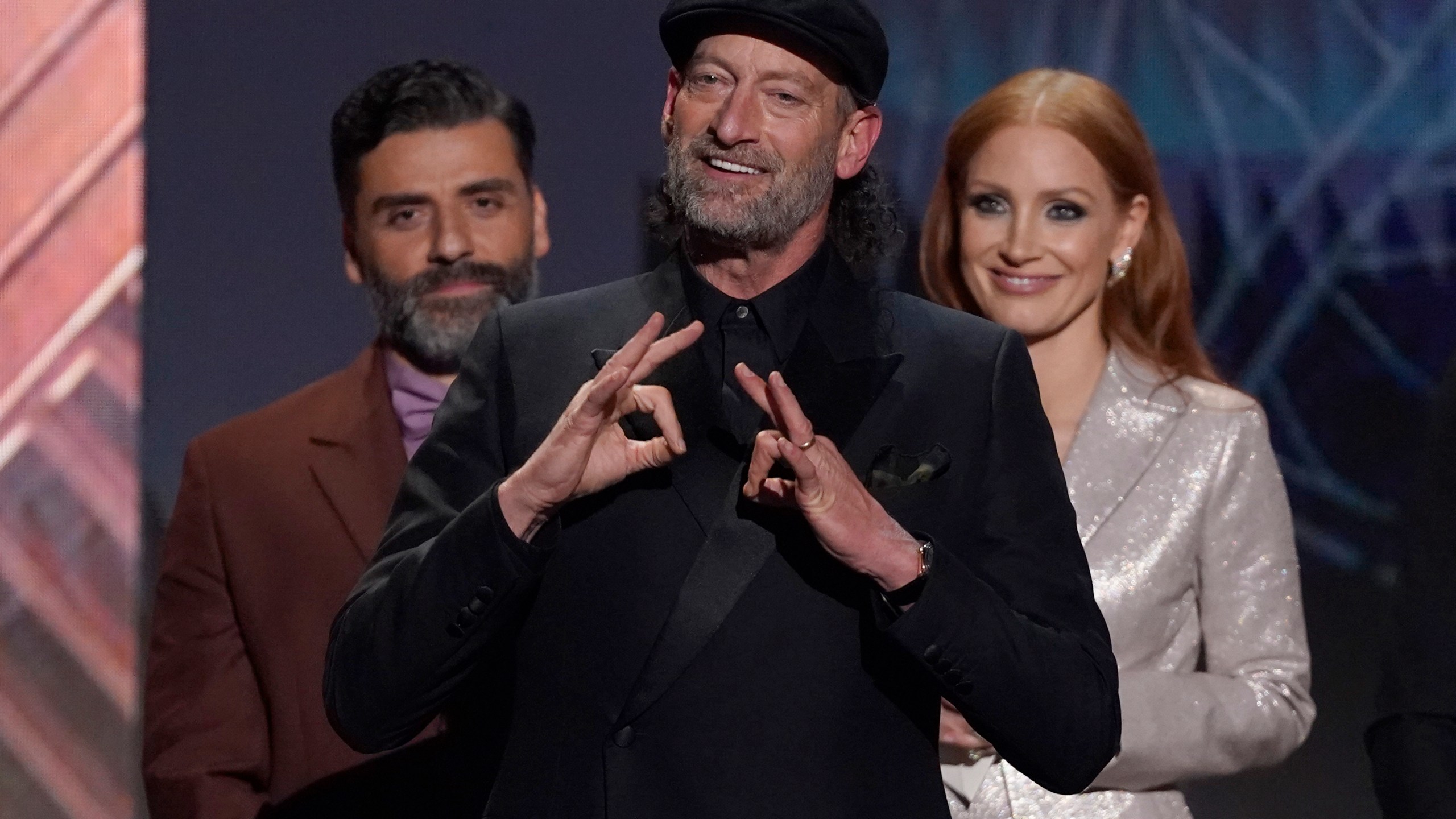 Troy Kotsur accepts the award for outstanding performance by a male actor in a supporting role for "CODA" at the 28th annual Screen Actors Guild Awards at the Barker Hangar on Sunday, Feb. 27, 2022, in Santa Monica, Calif. Oscar Isaac, left, and Jessica Chastain look on from behind. (AP Photo/Chris Pizzello)