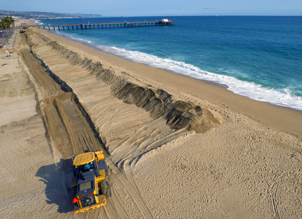 Workers build a sand berm to prevent flooding north of the Balboa Pier during high tide in Newport Beach, Calif., on Thursday, Aug. 19, 2021. According to a U.S. federal report released on Tuesday, Feb. 15, 2022, seas lapping against America’s coastlines are rising ever faster and will be 10 to 12 inches higher by the year 2050 with major U.S. Eastern cities regularly hit with costly sunny day flooding. (Jeff Gritchen/The Orange County Register via AP)