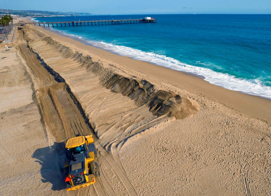 Workers build a sand berm to prevent flooding north of the Balboa Pier during high tide in Newport Beach, Calif., on Thursday, Aug. 19, 2021. According to a U.S. federal report released on Tuesday, Feb. 15, 2022, seas lapping against America’s coastlines are rising ever faster and will be 10 to 12 inches higher by the year 2050 with major U.S. Eastern cities regularly hit with costly sunny day flooding. (Jeff Gritchen/The Orange County Register via AP)