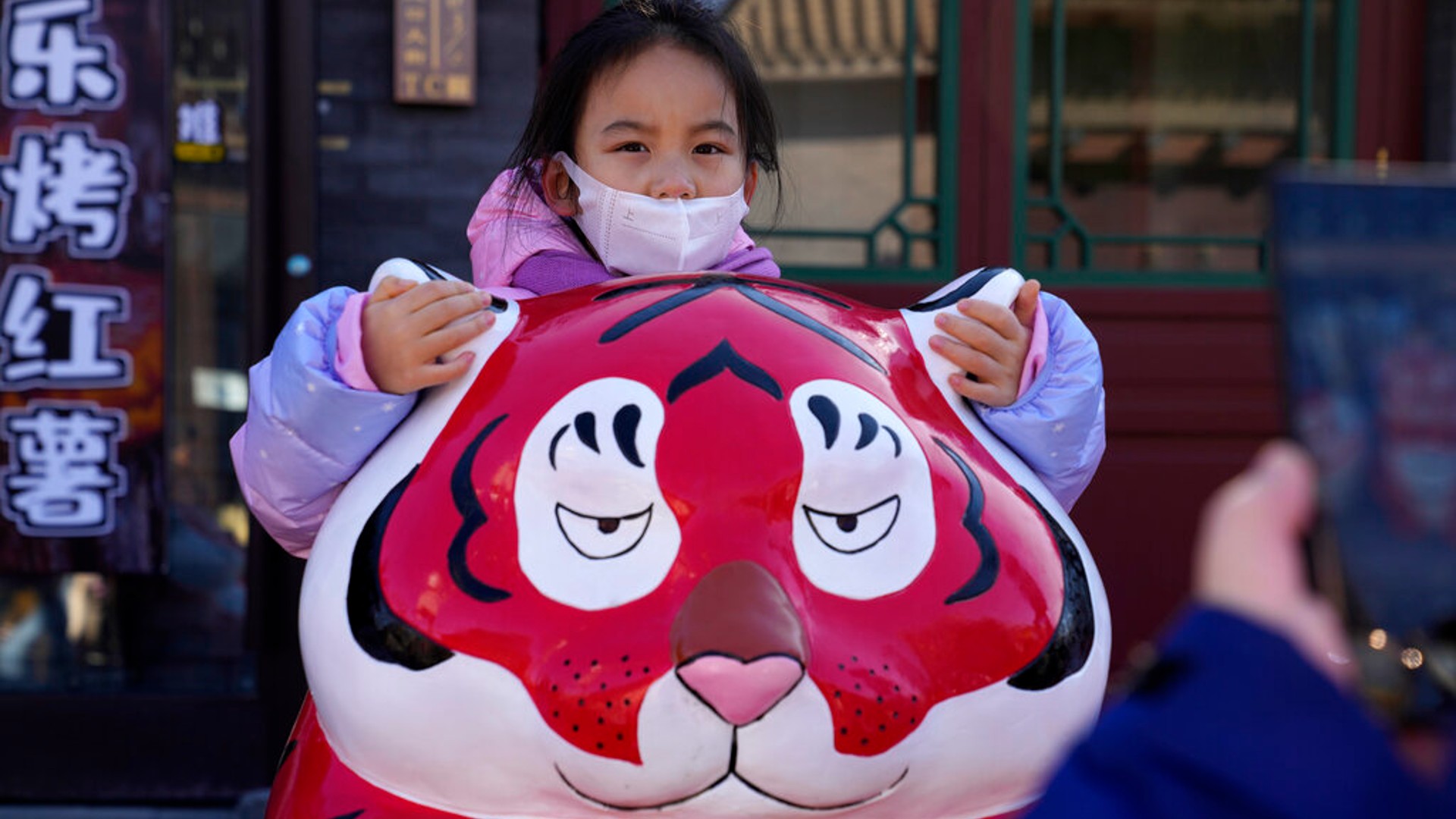 A child wearing a mask holds on to the ears of a Tiger sculpture on the first day of the Lunar Year of the Tiger in Beijing, China, Tuesday, Feb. 1, 2022. (AP Photo/Ng Han Guan)