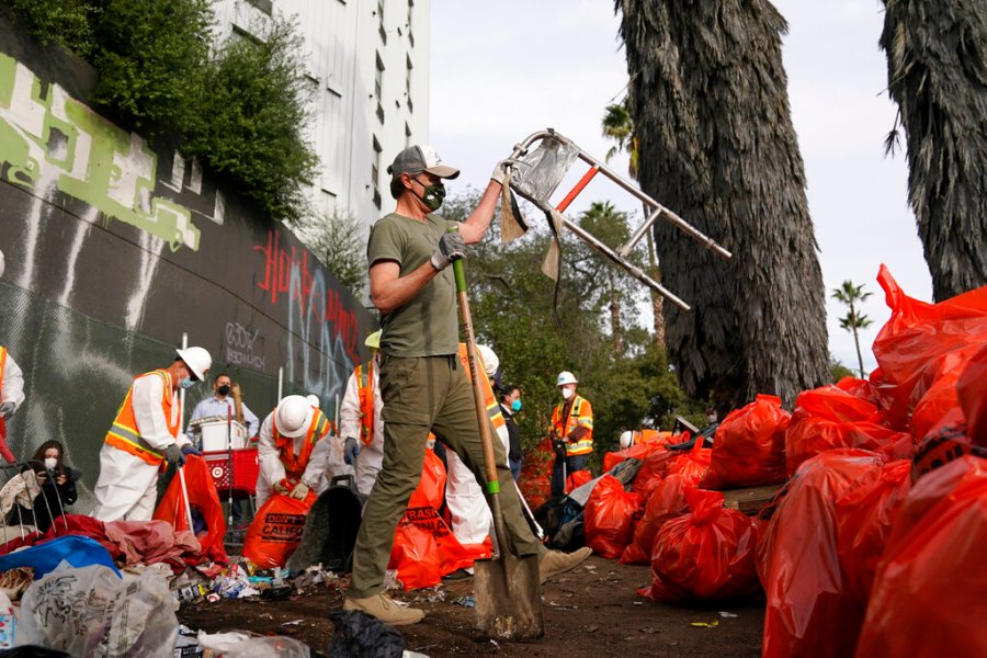 California Gov. Gavin Newsom, center, helps clean a homeless encampment alongside a freeway on Jan. 12, 2022, in San Diego. California's governor proposed a plan on Thursday, March 3, 2022, to force homeless people with severe mental health and addiction disorders into treatment. (AP Photo/Gregory Bull, File)