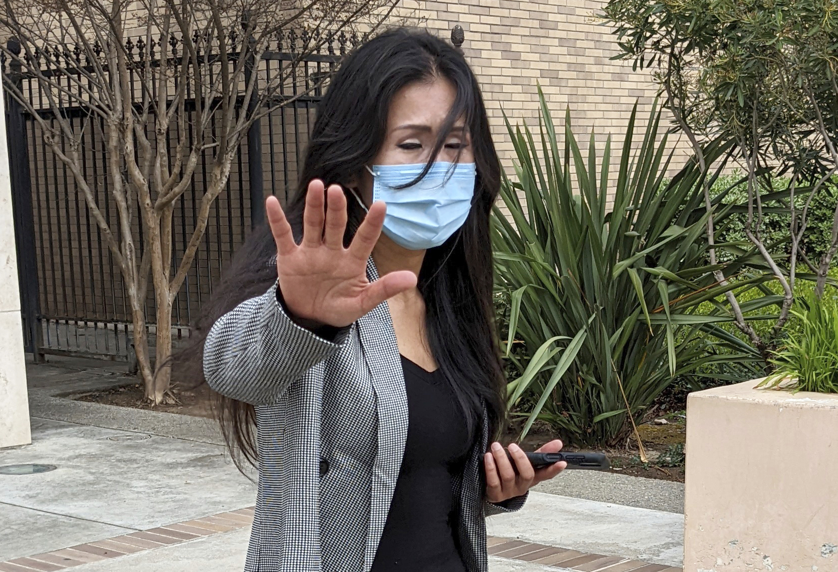 Julie Lee Choi waves off reporters outside Santa Clara Superior Court in San Jose, Calif., on Tuesday, March 29, 2022. Choi, accused of harassing Apple CEO Tim Cook with pleas for sex and other crude suggestions before showing up at his Silicon Valley home last autumn and suggesting she could become violent agreed to stay way from him for the next three years under an agreement approved Tuesday. (AP Photo/Michael Liedtke)