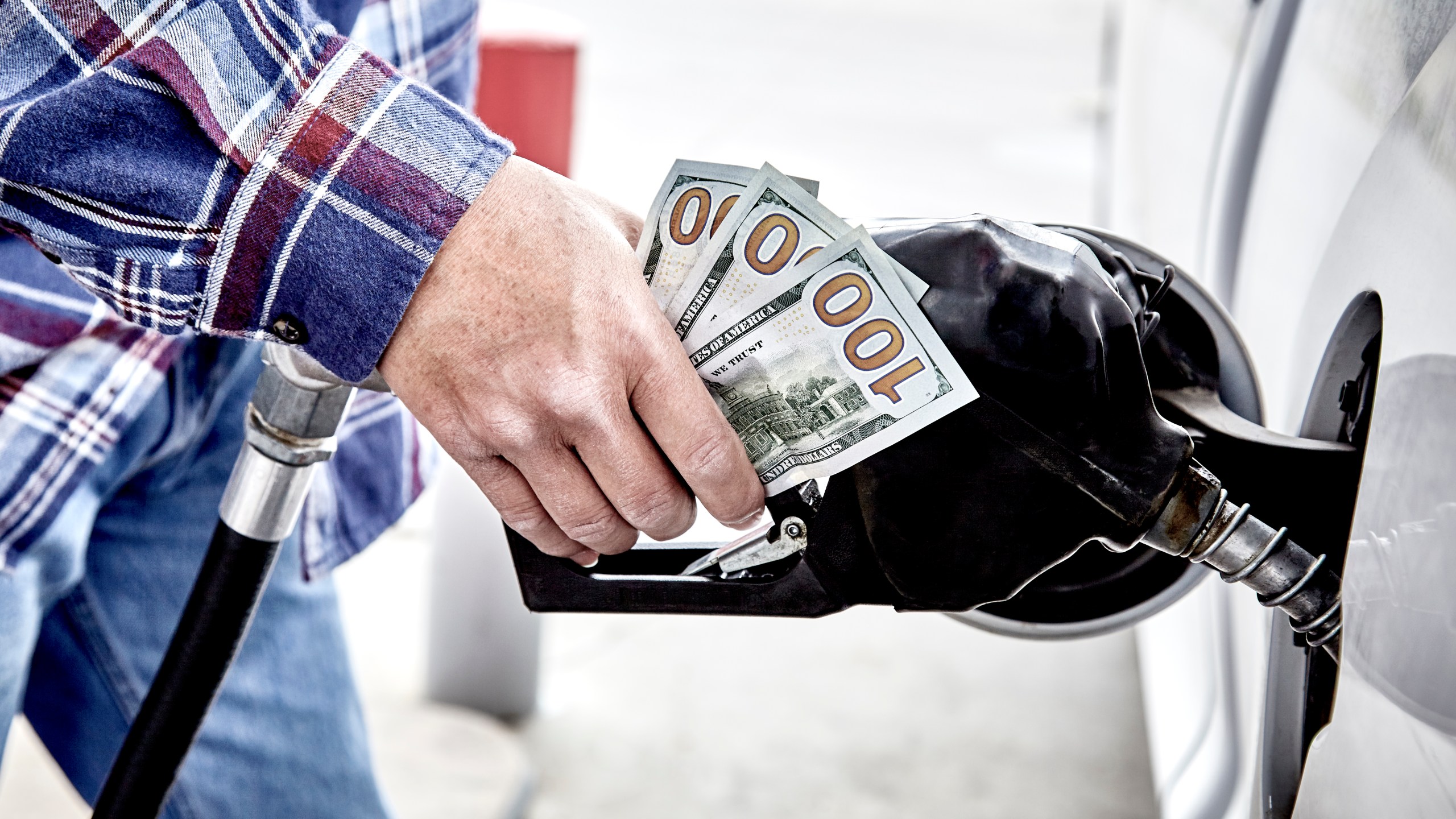 A man holds hundred dollar bills while pumping gas in this undated file photo. (Getty Images)