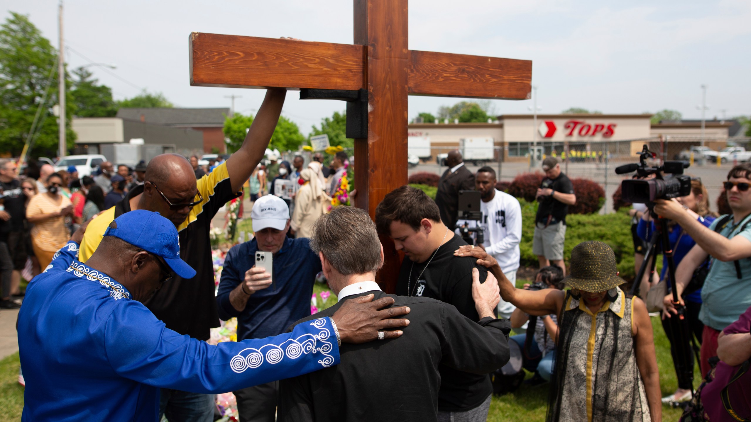 A group prays at the site of a memorial for the victims of the Buffalo supermarket shooting outside the Tops Friendly Market on Saturday, May 21, 2022, in Buffalo, N.Y. Tops was encouraging people to join its stores in a moment of silence to honor the shooting victims Saturday at 2:30 p.m., the approximate time of the attack a week earlier. Buffalo Mayor Byron Brown also called for 123 seconds of silence from 2:28 p.m. to 2:31 p.m., followed by the ringing of church bells 13 times throughout the city to honor the 10 people killed and three wounded. (AP Photo/Joshua Bessex)