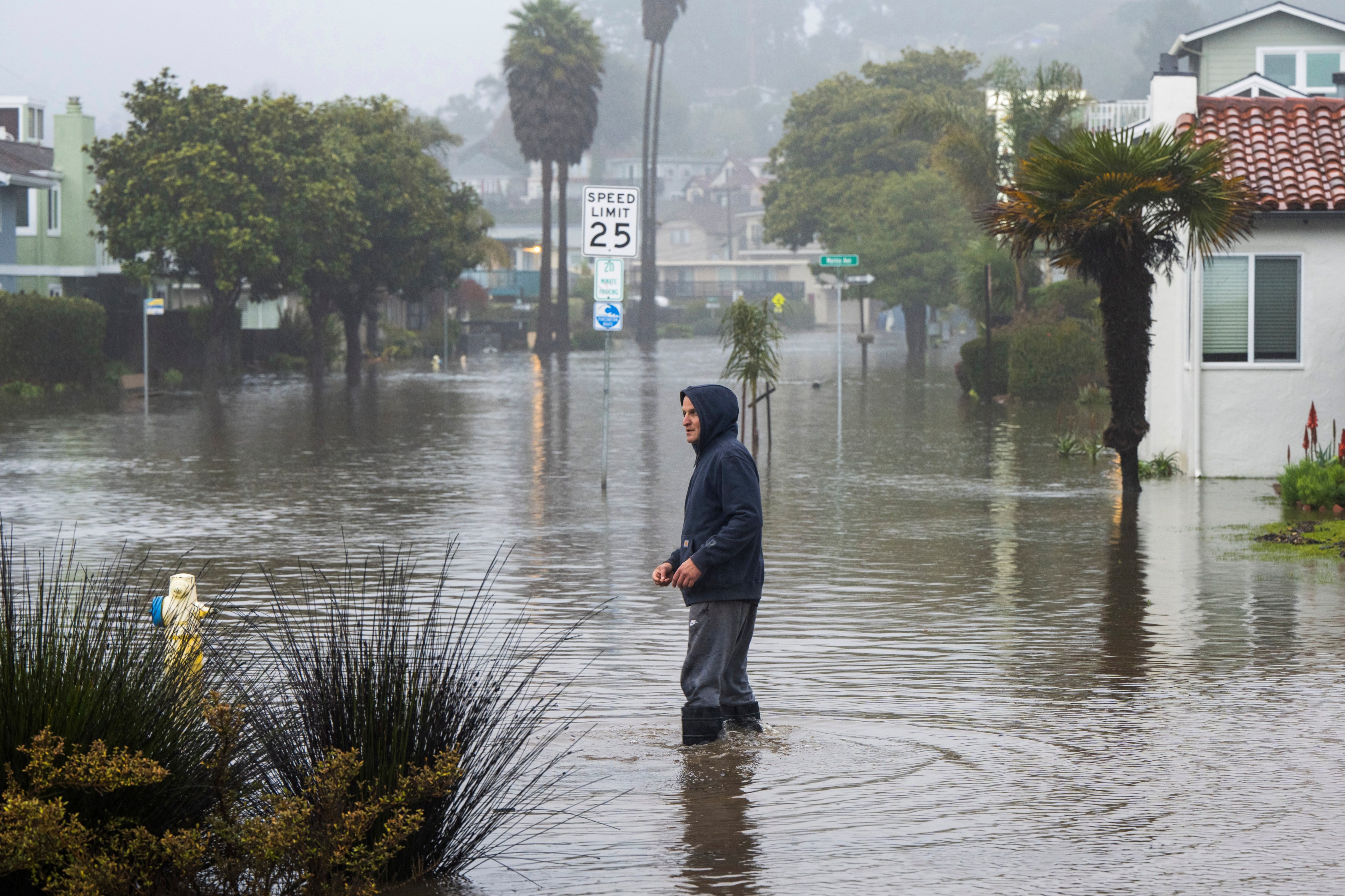 A man wades through a flooded street in the Rio Del Mar neighborhood of Aptos, Calif. on Jan. 9, 2023. (Nic Coury/Associated Press)