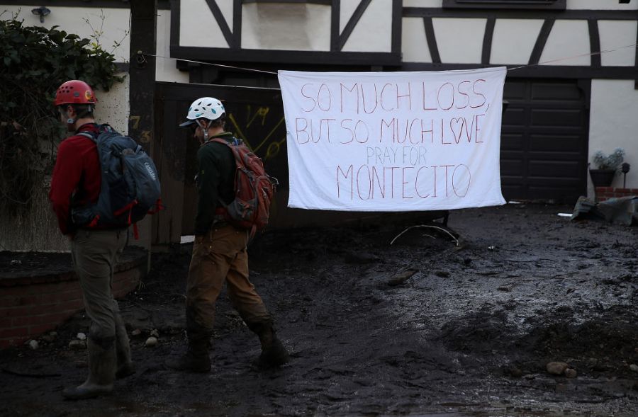 People walk by a homemade sign that hangs in front of a home after a mudslide on January 10, 2018 in Montecito, California. 17 people have died and hundreds hundreds of homes have been destroyed or damaged after massive mudslides crashed through Montecito, California early Tuesday morning.  (Photo by Justin Sullivan/Getty Images)