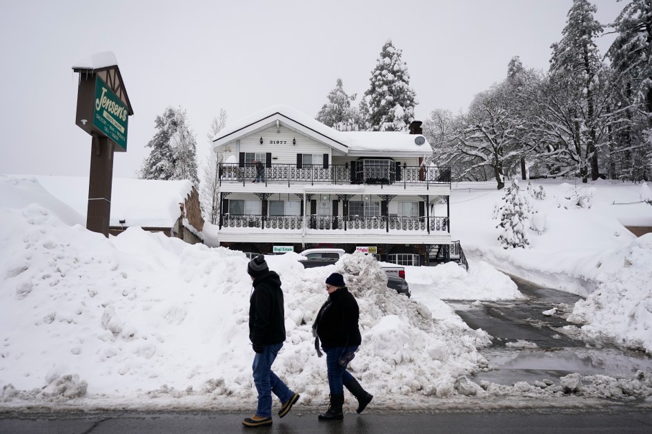 Two residents walk past the piles of snow in Running Springs, Calif. on Feb. 28, 2023. (Jae C. Hong/As