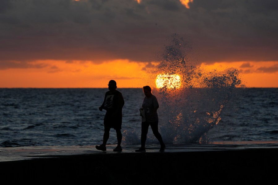 FILE - The sun rises above the Atlantic Ocean as waves crash near beach goers walking along a jetty, Dec. 7, 2022, in Bal Harbour, Fla. The world's oceans have suddenly spiked much hotter and well above record levels, with scientists trying to figure out what it means and whether it forecasts a surge in atmospheric warming. (AP Photo/Wilfredo Lee, File)