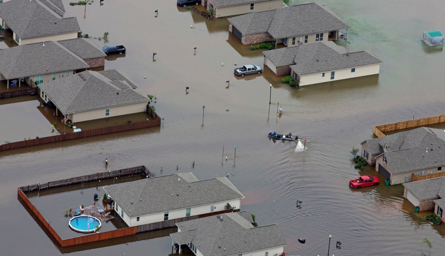 FILE- A boat motors between flooded homes after heavy rains inundating the region, in Hammond, La., on Aug. 13, 2016. A new study Thursday, May 18, 2023, finds the natural burst of El Nino warming that changes weather worldwide is far costlier with longer-lasting expenses than experts had thought, averaging trillions of dollars in damage. (AP Photo/Max Becherer, File)