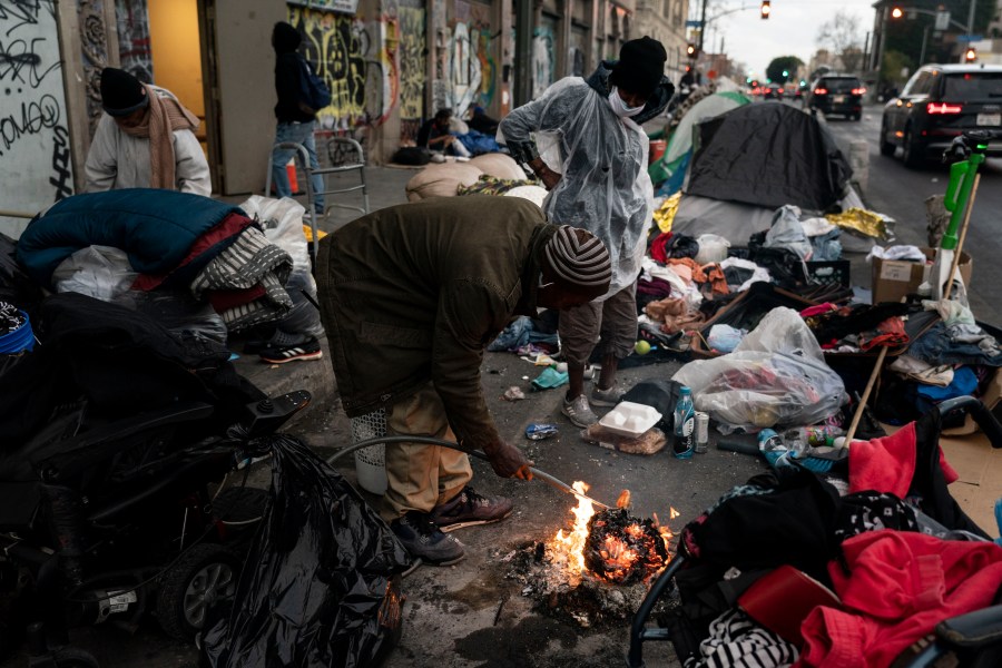 FILE - Robert Mason, a 56-year-old homeless man, warms up a piece of doughnut over a bonfire he set to keep himself warm on Skid Row in Los Angeles, Tuesday, Feb. 14, 2023. Five major U.S. cities and the state of California will receive federal help to get unsheltered residents into permanent housing under a new plan announced Thursday, May 18, 2023, as part of the Biden administration's larger goal to reduce homelessness 25% by 2025. (AP Photo/Jae C. Hong, File)