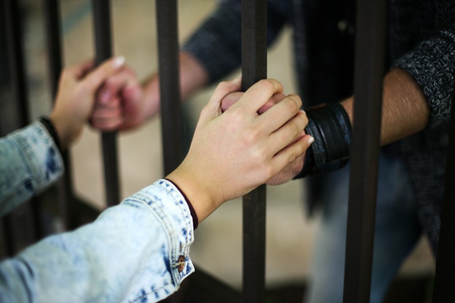 This file image shows a couple holding hands on opposite sides of prison bars