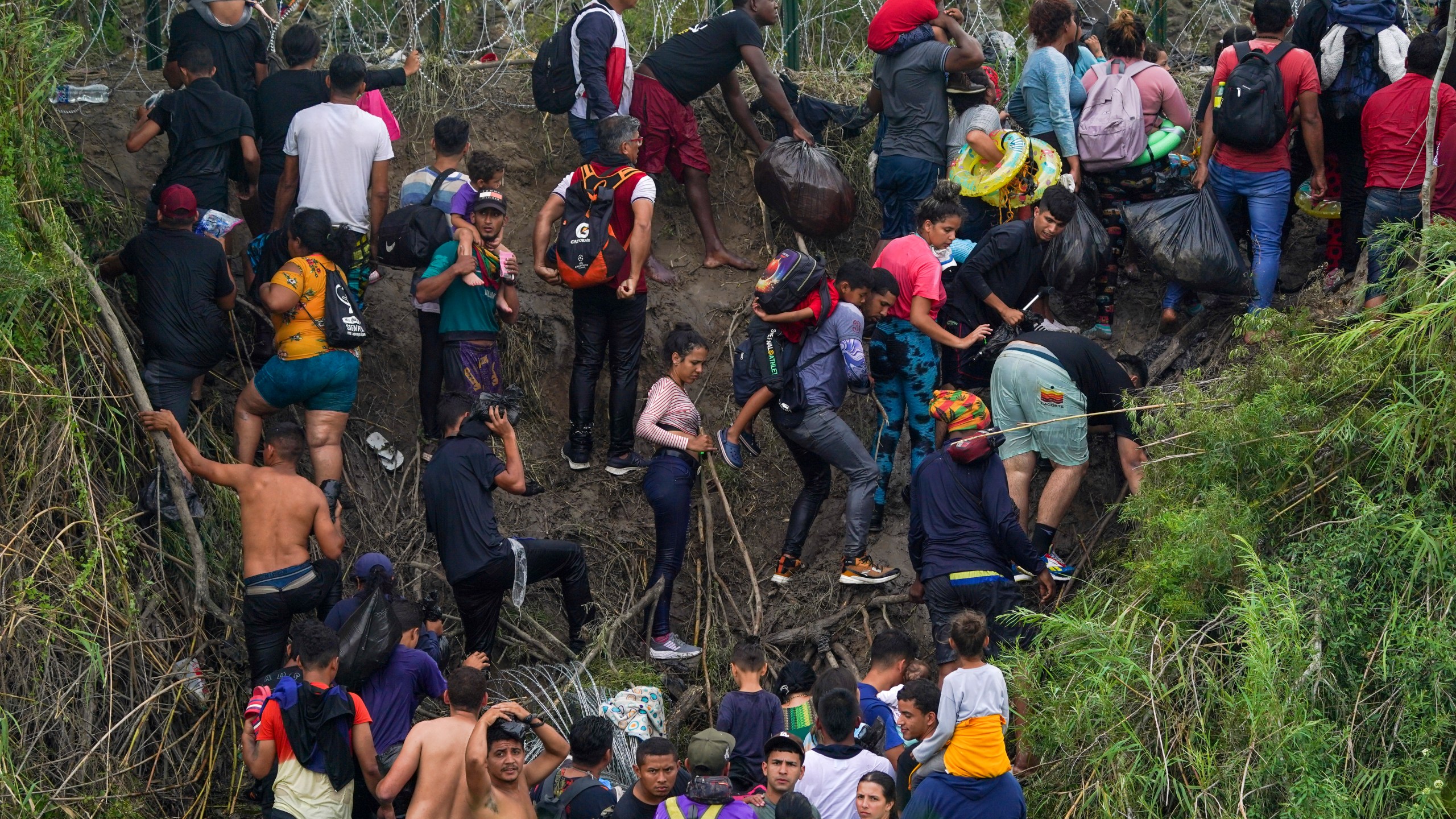 Migrants stand on the bank of the Rio Grande river as Texas National Guards block them from behind razor wire, seen from Matamoros, Mexico, Thursday, May 11, 2023. Pandemic-related U.S. asylum restrictions, known as Title 42, are to expire May 11. (AP Photo/Fernando Llano)