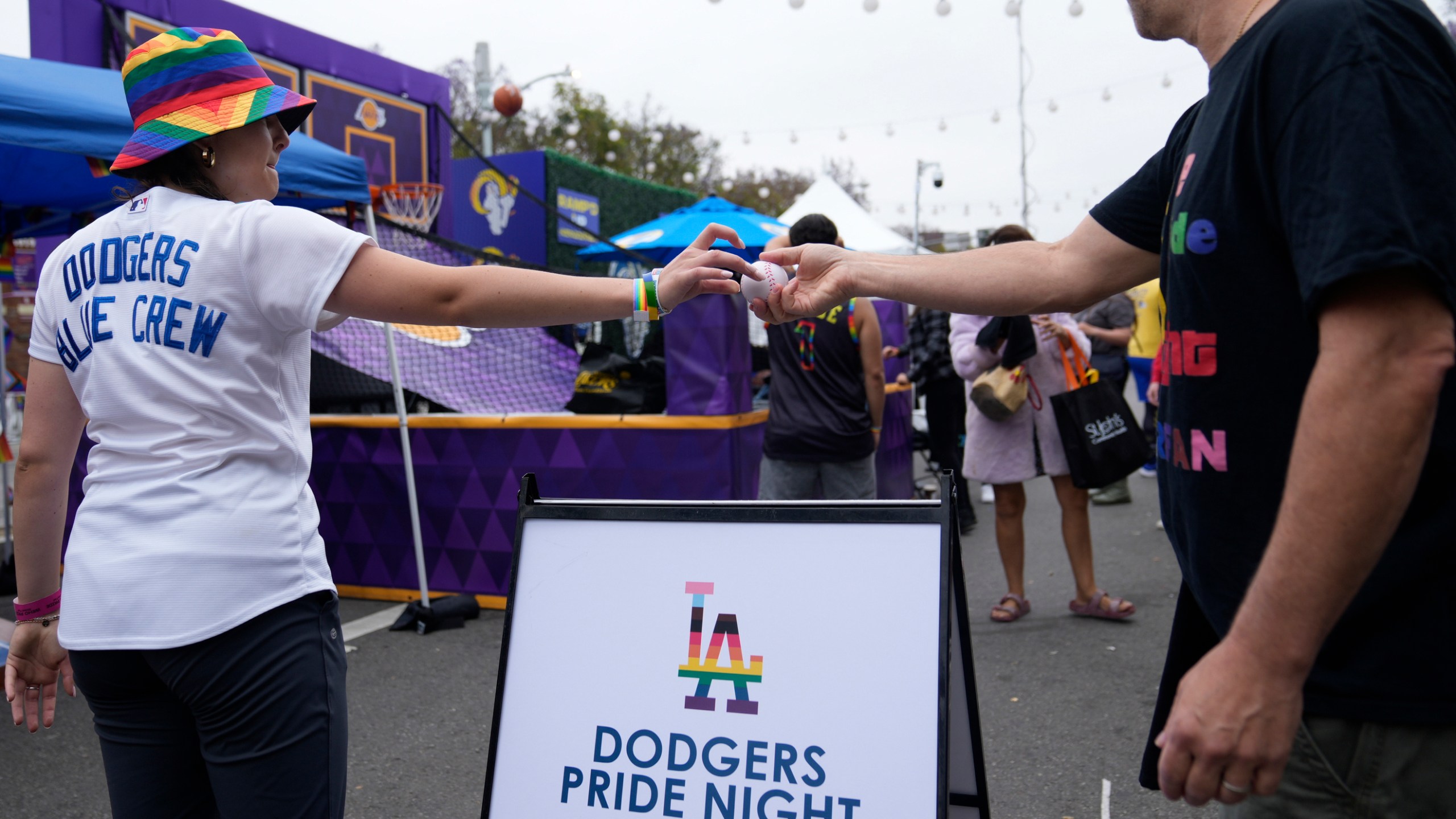 FILE - A Los Angeles Dodgers Pride promoter gives a ball to a participant at the WeHo Pride Parade in West Hollywood, Calif., on Sunday, June 4, 2023. Under a barrage of criticism from some conservative Catholics, the team rescinded an invitation to a satirical LGBTQ+ group called the Sisters of Perpetual Indulgence to be honored at the 2023 Pride Night. A week later, after a vehement backlash from LGBTQ+ groups and their allies, the Dodgers reversed course — re-inviting the Sisters’ Los Angeles chapter to be honored for its charity work and apologizing to the LGBTQ+ community. (AP Photo/Damian Dovarganes, File)