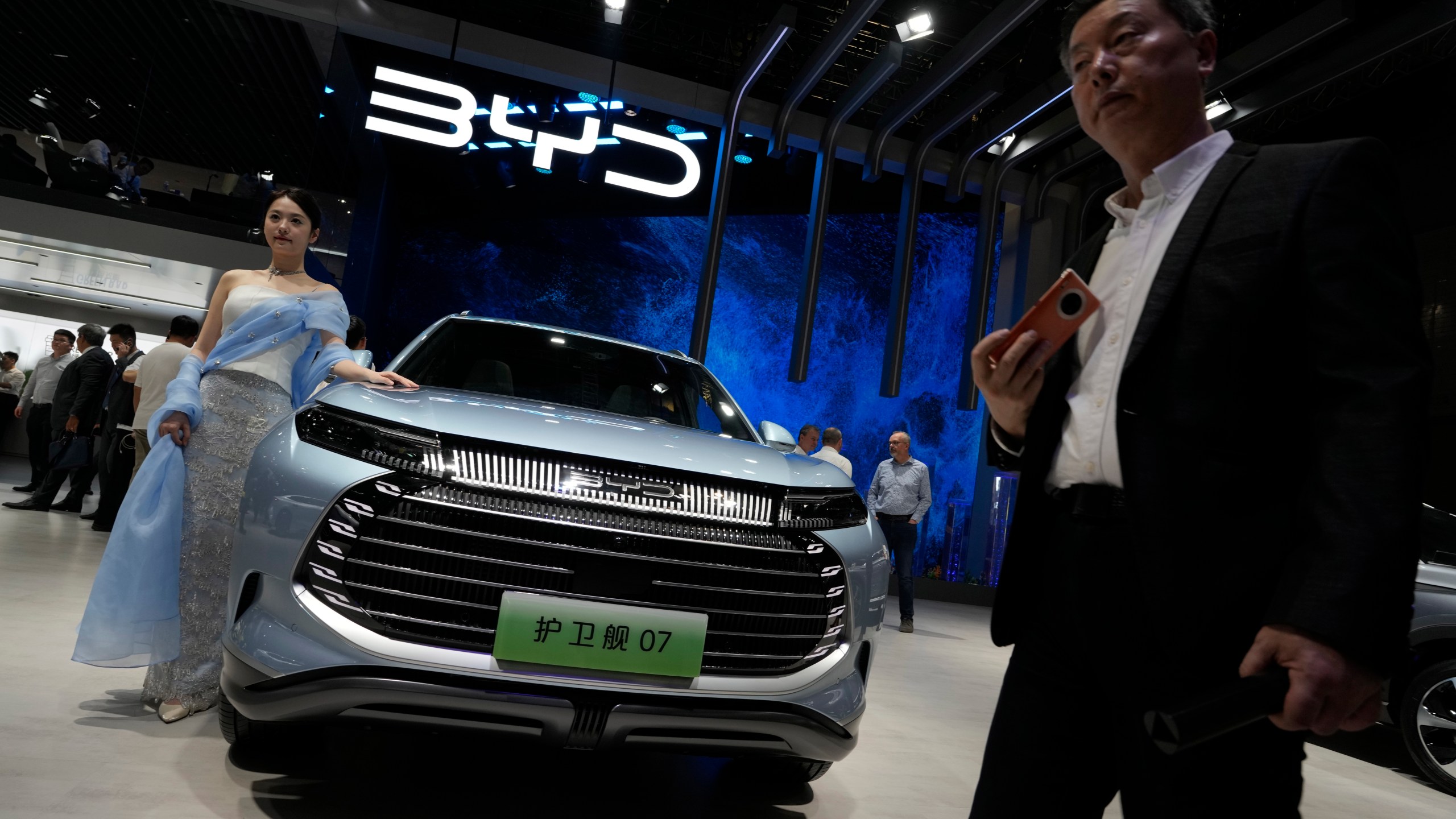 A model stands next to a car from BYD during the Shanghai auto show in Shanghai, on April 18, 2023. Threatened by possible shortages of lithium for electric car batteries, automakers are racing to lock in supplies of the once-obscure "white gold" in a politically and environmentally fraught competition from China to Nevada to Chile. General Motors Co. and the parent company of China's BYD Auto Ltd. went straight to the source and bought stakes in lithium miners, a rare step in an industry that relies on outside vendors for copper and other raw materials. (AP Photo/Ng Han Guan)