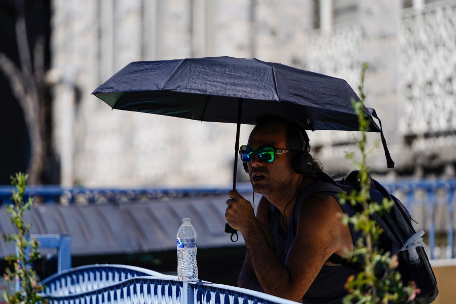 A man uses an umbrella to avoid the midday sun.