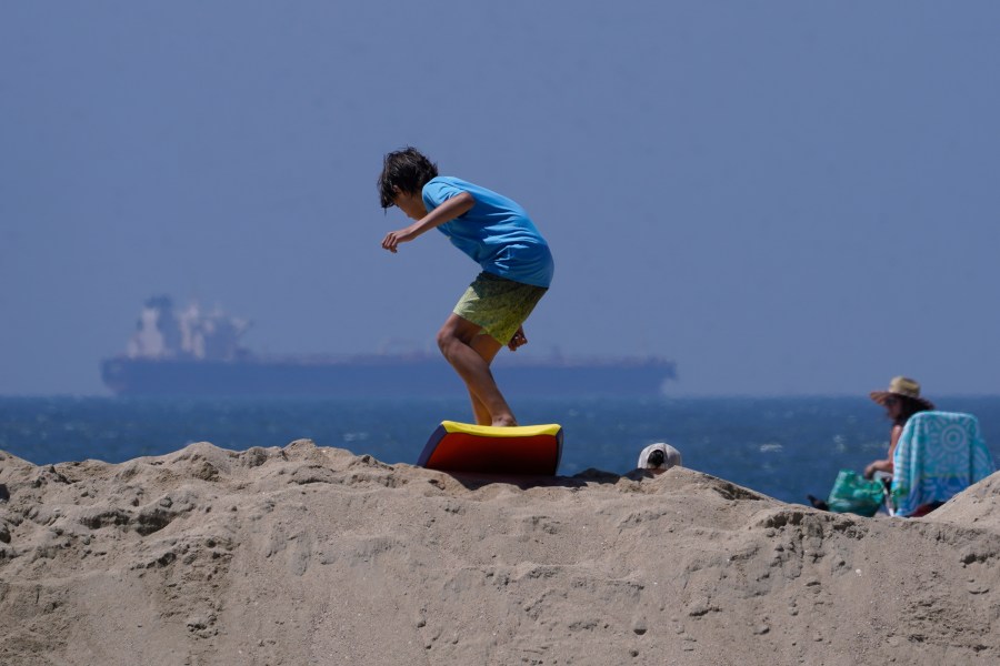 A boy slides with a surf board on top of a sand berm in Seal Beach, Calif., Friday, Aug. 18, 2023. Officials in Southern California were also re-enforcing sand berms, built to protect low-lying coastal communities against winter surf. Hurricane Hilary is churning off Mexico's Pacific coast as a powerful Category 4 storm threatening to unleash torrential rains on the mudslide-prone border city of Tijuana before heading into Southern California as the first tropical storm there in 84 years. (AP Photo/Damian Dovarganes)