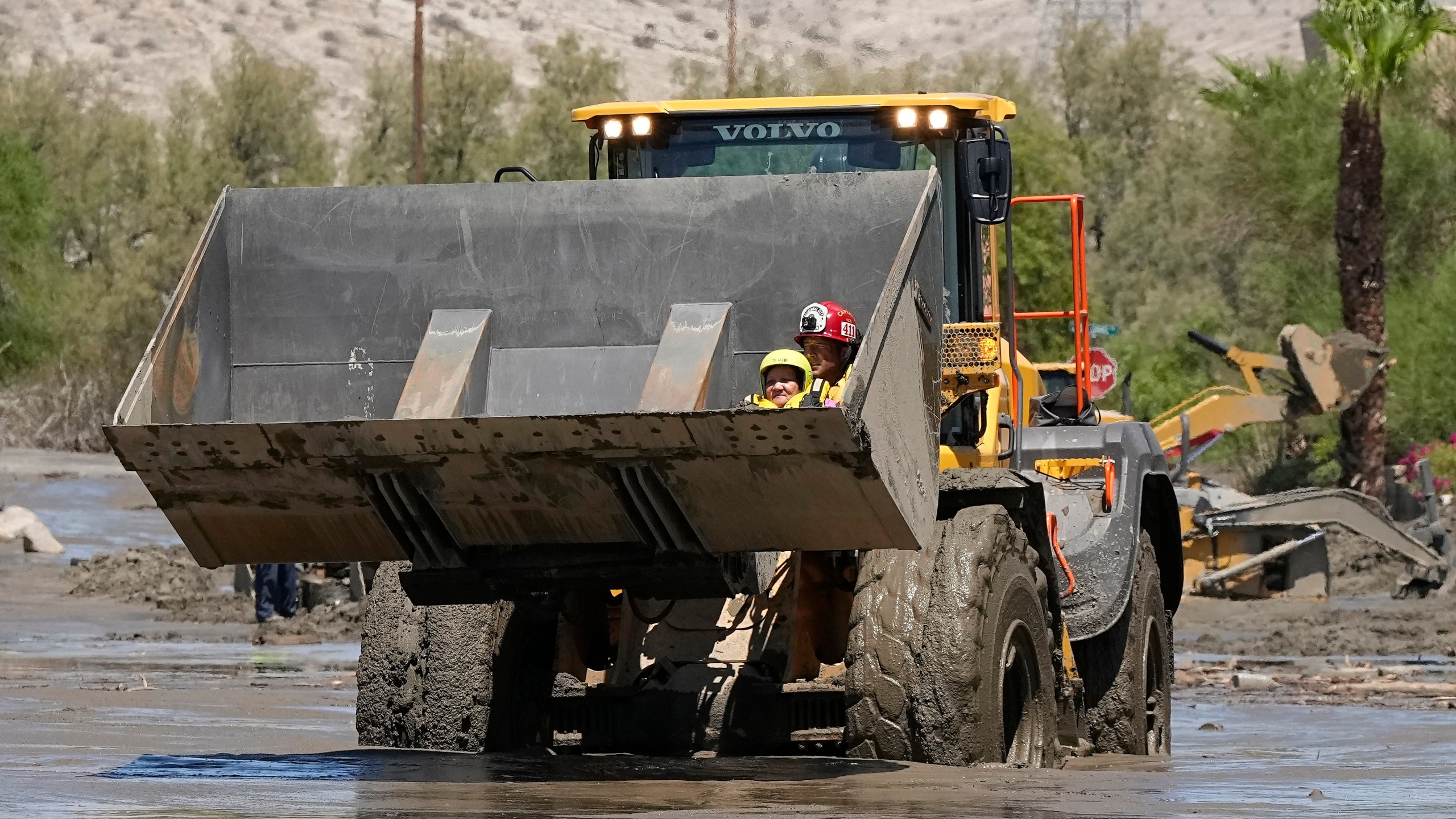 Firefighters use a skip loader to rescue a person from an assisted living center after the street was flooded with mud Monday, Aug. 21, 2023, in Cathedral City, Calif. Forecasters said Tropical Storm Hilary was the first tropical storm to hit Southern California in 84 years, bringing the potential for flash floods, mudslides, isolated tornadoes, high winds and power outages. (AP Photo/Mark J. Terrill)