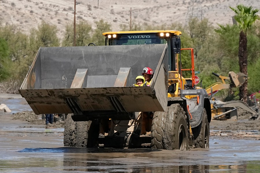 Firefighters use a skip loader to rescue a person from an assisted living center after the street was flooded with mud Monday, Aug. 21, 2023, in Cathedral City, Calif. Forecasters said Tropical Storm Hilary was the first tropical storm to hit Southern California in 84 years, bringing the potential for flash floods, mudslides, isolated tornadoes, high winds and power outages. (AP Photo/Mark J. Terrill)