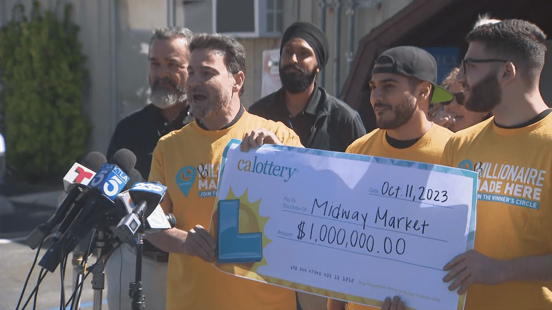 Owner Andy Khalil (left) holds a check for $1 million after a winning Powerball ticket was sold at his Midway M