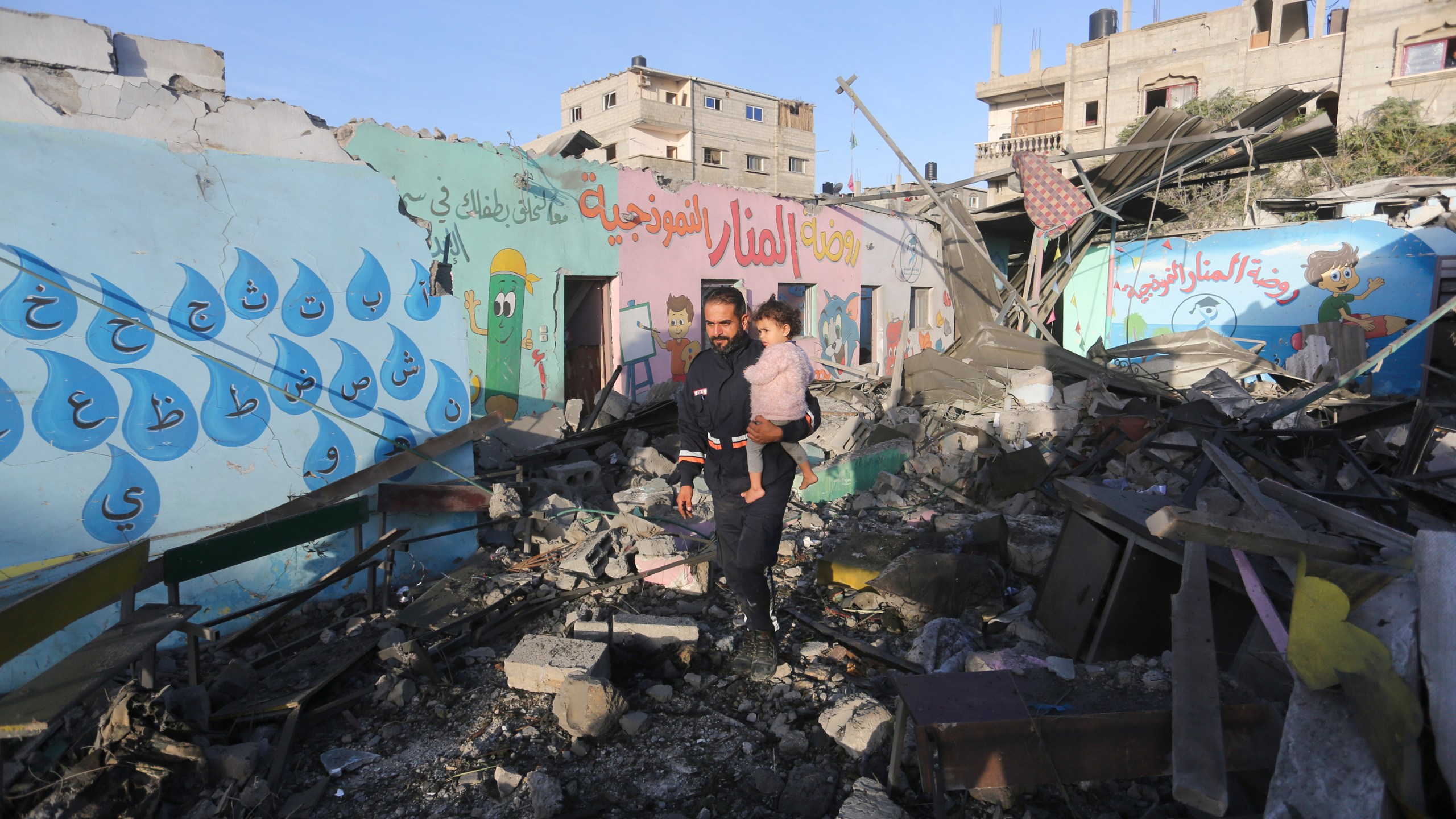 Palestinians walk by a building destroyed in Israeli bombardment overnight in Rafah, Gaza Strip, Friday, Nov. 24, 2023. (AP Photo/Hatem Ali)