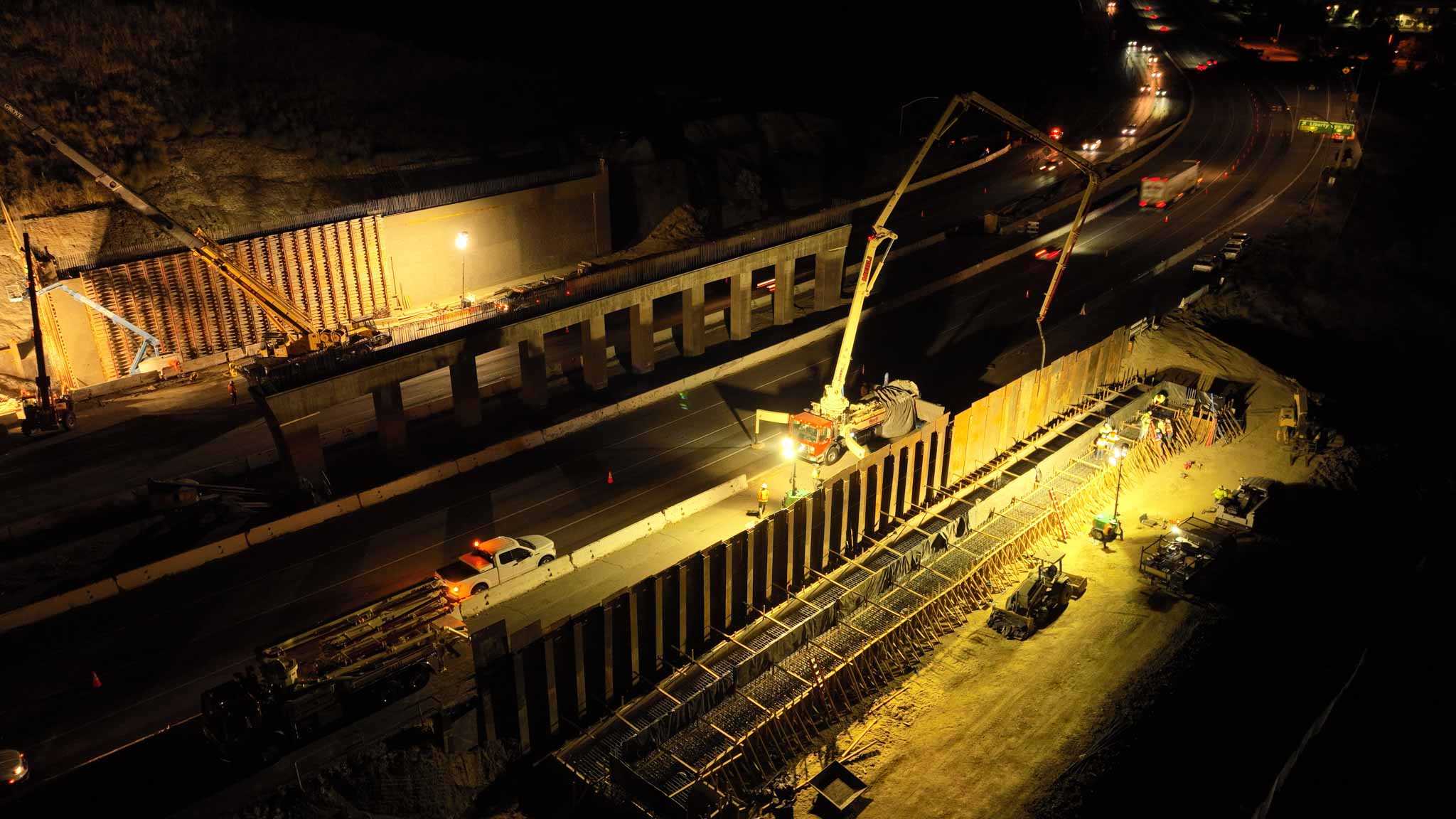 An aerial photo taken at night showing where crews are placing hundreds of tons of wet concrete for the foundation of the abutment, or bridge wall, next to the southbound lanes of US Highway 101 near Liberty Canyon Road in Agoura Hills, California, to build the Wallis Annenberg Wildlife Crossing. (Caltrans)