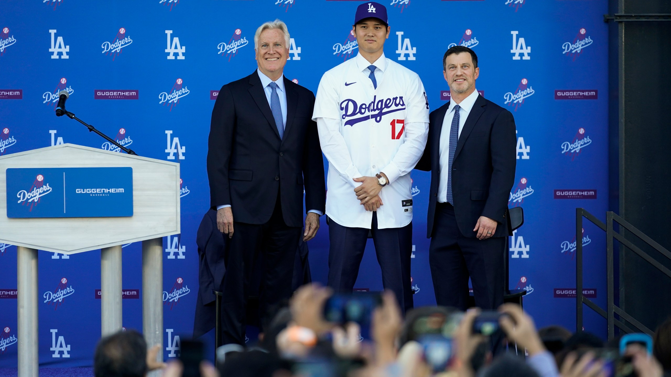 Los Angeles Dodgers' Shohei Ohtani, center, poses for a photo with owner and chairman Mark Walter, left, and president of baseball operations Andrew Friedman applaud during a news conference at Dodger Stadium Thursday, Dec. 14, 2023, in Los Angeles. (AP Photo/Ashley Landis)