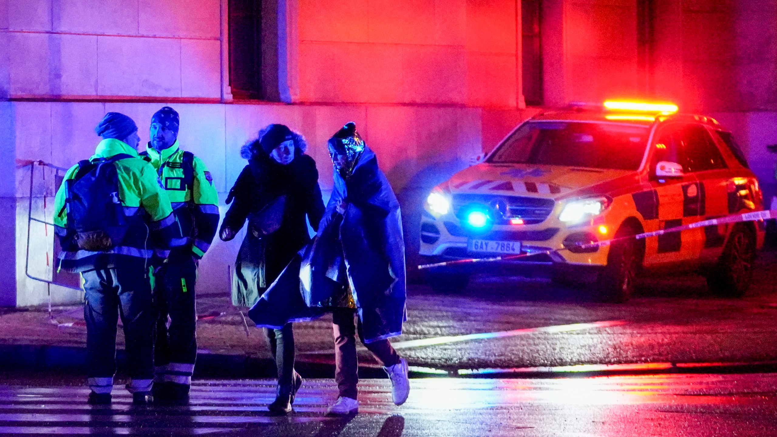 People, one wrapped in a thermal blanket, walk near the building of Philosophical Faculty of Charles University in downtown Prague, Czech Republic, Thursday, Dec. 21, 2023. A mass shooting in downtown Prague killed several people and injured others, and the person who opened fire also is dead, Czech police and the city's rescue service said Thursday. (AP Photo/Petr David Josek)