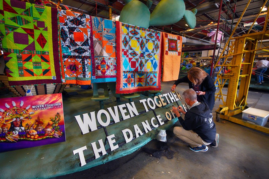 Carrie Holland joined by her husband Jim Holland works on a sign that reads "Woven Together The Dance of Life" on the OneLegacy Donate Life Rose Parade Float in Irwindale, Calif. on Tuesday, Dec. 26, 2023. (AP Photo/Richard Vogel)
