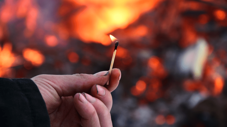 A man holding a burning match with a large fire in the background is seen in this file image.