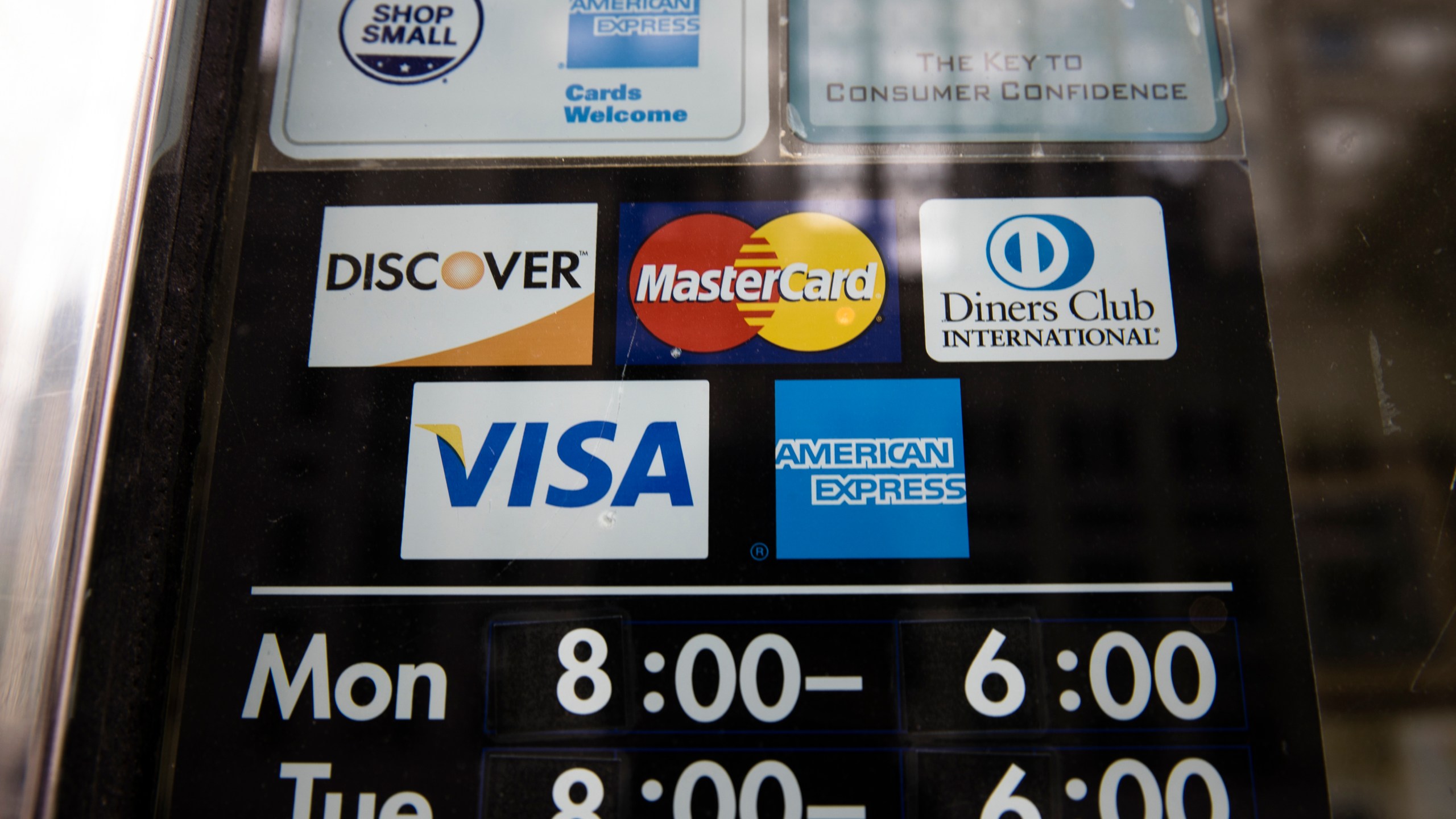 File - Credit card options are shown on a store's door on Nov. 29, 2018 in Philadelphia. Noticeable pockets of Americans are quickly running up their credit card balances and increasing numbers are now falling behind on their debts. (AP Photo/Matt Rourke, File)