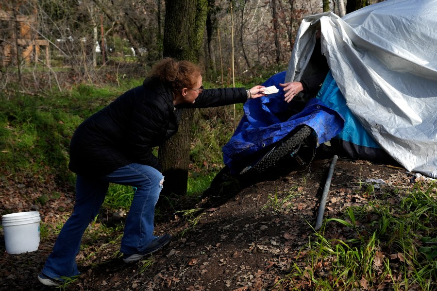 Resiliency Empowerment Support Team (REST) team member Beth Perkins, give a homeless person a hand warmer during a visit to a homeless camp in Chico, Calif., Feb. 8, 2024. A measure aimed at transforming how California spends money on mental health will go before voters in March as the state continues to grapple an unabated homelessness crisis. The REST Program does daily visits to homeless encampments to get them into treatment or housing. Butte County officials fear the REST program would lose its funding if California voters approve Proposition 1.(AP Photo/Rich Pedroncelli)