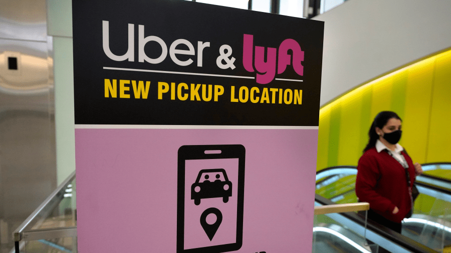 In this Feb. 9, 2021 file photo, a passer-by walks past a sign offering directions to an Uber and Lyft ride pickup location at Logan International Airport, in Boston.