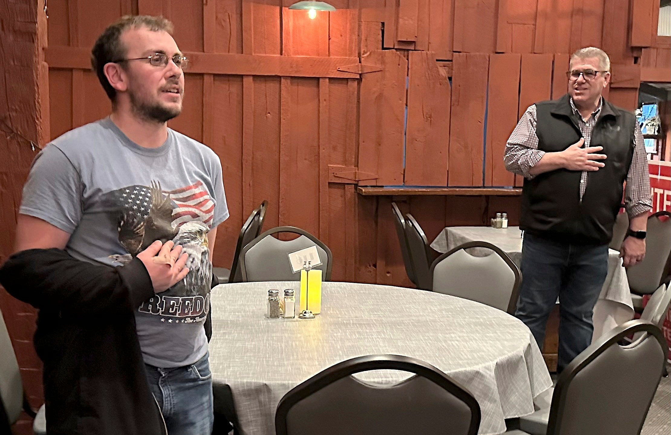 Congressional candidate Darren Bailey, right, leads the Pledge of Allegiance at a campaign stop with the help of Casey resident Brandon Baston and his American flag T-shirt, Tuesday, Feb. 27, 2024 in Casey, ill. Bailey, a former state senator and 2022 Republican nominee for governor, is running in the March 19th primary to unseat fellow GOP Congressman Mike Bost, a five-term incumbent who has the endorsement of former President Donald Trump, in Illinois' 12th District, which encompasses the bottom one-third of Illinois. (AP Photo/John O'Connor)