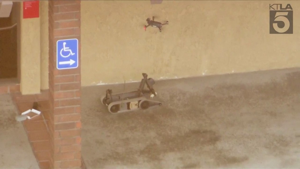 A remote-controlled robot and drone investigate possible suspicious devices near the suspect on March 26, 2024. (KTLA)